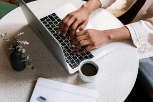 Person typing on laptop keyboard. A cup of coffee on the table next to them.